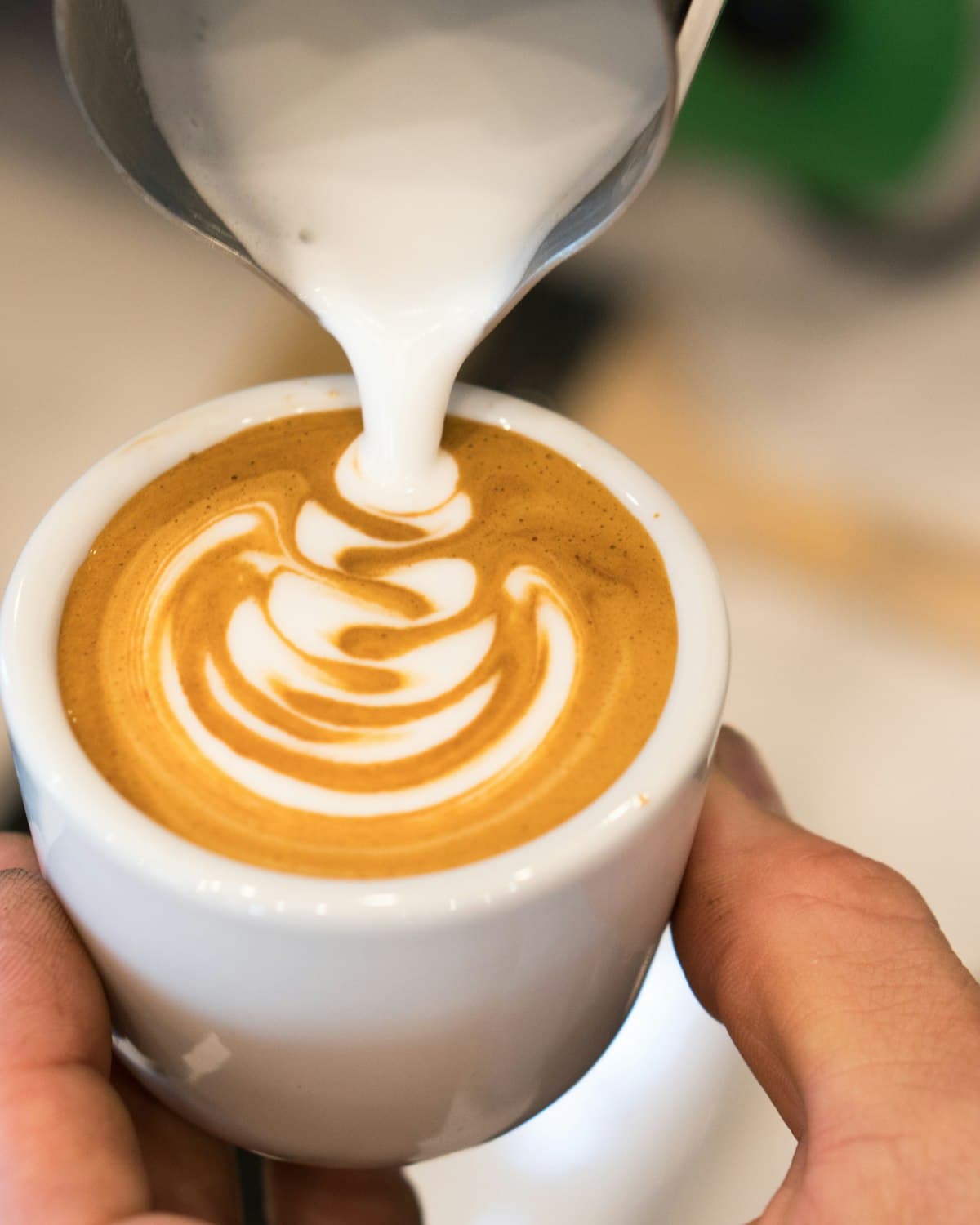 Barista pouring steamed milk into a cappuccino, forming latte art
